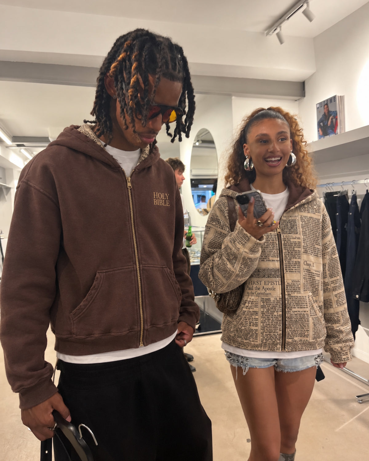 Two people wearing both sides of the HOLY zip-up in a clothing store
